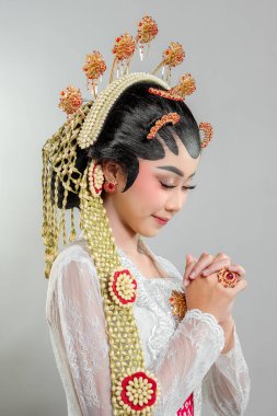 Solo Putri 'de altın yasemin aksesuarları ve beyaz dantelli kebaya ile süslenmiş Endonezyalı bir gelin. Zarif bir şekilde gülümseyerek poz veriyor. Cava güzelliği yayıyor..