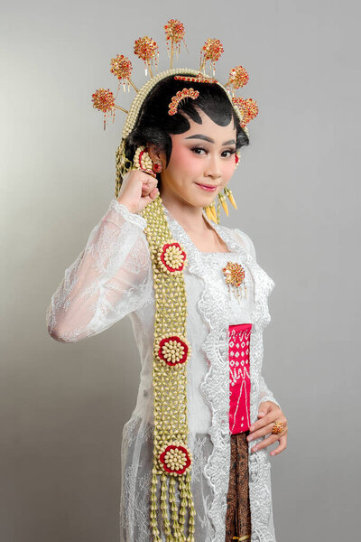 Indonesian bride in Solo Putri attire, wearing a golden headdress and jasmine garland. She poses with a soft smile and confident gesture, radiating elegance and tradition.