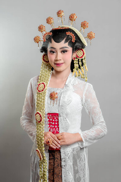 An elegant Indonesian bride in Solo Putri traditional attire, wearing a golden headdress, jasmine garlands, and intricate lace kebaya, radiating grace with a warm smile.