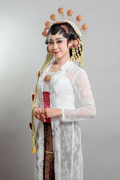 An elegant Indonesian bride in Solo Putri traditional attire, wearing a golden headdress, jasmine garlands, and intricate lace kebaya, radiating grace with a warm smile.