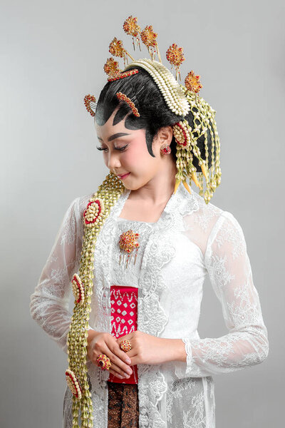 An elegant Indonesian bride in Solo Putri traditional attire, wearing a golden headdress, jasmine garlands, and intricate lace kebaya, radiating grace with a warm smile.