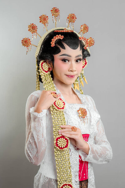 Indonesian bride in Solo Putri attire, wearing a golden headdress, jasmine garlands, and intricate lace kebaya. She radiates beauty and confidence with a gentle smile.