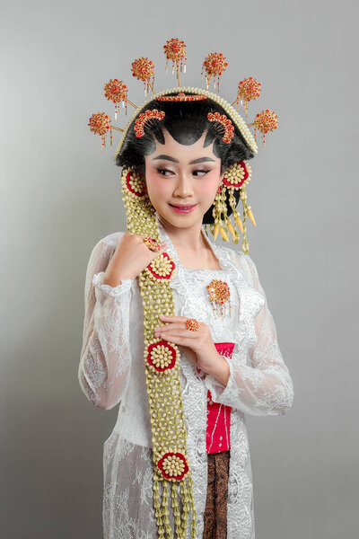 Indonesian bride in Solo Putri attire, wearing a golden headdress, jasmine garlands, and intricate lace kebaya. She radiates beauty and confidence with a gentle smile.