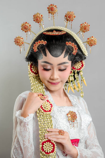 Indonesian bride in Solo Putri attire, wearing a golden headdress, jasmine garlands, and intricate lace kebaya. She radiates beauty and confidence with a gentle smile.