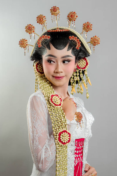 Indonesian bride in Solo Putri attire, wearing a golden headdress, jasmine garlands, and intricate lace kebaya. She exudes grace and elegance with a soft, charming smile.