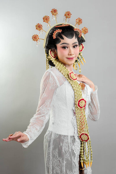 Indonesian bride in Solo Putri attire, wearing a golden headdress, jasmine garlands, and a white lace kebaya. She radiates grace and elegance with a soft, confident smile.