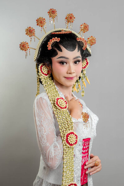 Indonesian bride in Solo Putri attire, wearing a golden headdress, jasmine garlands, and intricate lace kebaya. She exudes grace and elegance with a soft, charming smile.