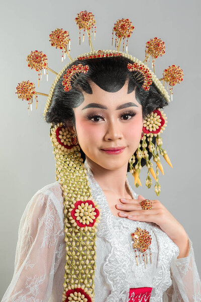 Indonesian bride in Solo Putri attire, wearing a golden headdress, jasmine garlands, and a white lace kebaya. She radiates grace and elegance with a soft, confident smile.