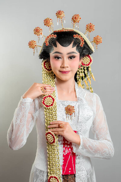 Indonesian bride in Solo Putri attire, wearing a golden headdress, jasmine garlands, and intricate lace kebaya. She exudes grace and elegance with a soft, charming smile.