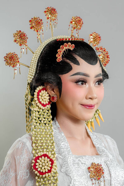 An elegant Indonesian bride in Solo Putri traditional attire, wearing a golden headdress, jasmine garlands, and intricate lace kebaya, radiating grace with a warm smile.
