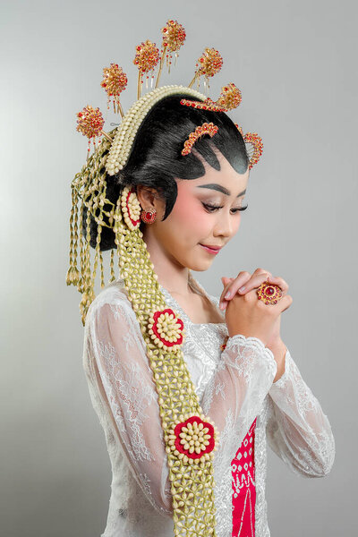 An Indonesian bride in Solo Putri attire, adorned with golden jasmine accessories and a white lace kebaya. She poses elegantly with a charming smile, exuding Javanese beauty.