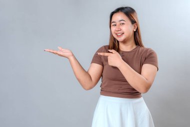 Gülümseyen genç bir kadın açık elini, promosyon içeriği, reklam afişleri veya pazarlama sunumları için uygun, davetkar ve dostane bir ifadeyle gösteriyor..