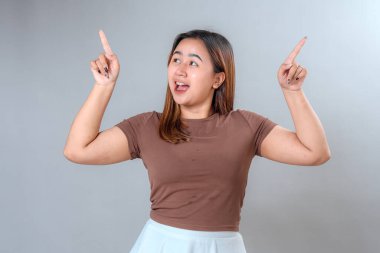 Her iki işaret parmağıyla yukarıya doğru gülümseyen neşeli genç bir kadın heyecan ve pozitiflik gösteriyor. Promosyon, reklam ve fotokopi alanı tasarımları için mükemmel.