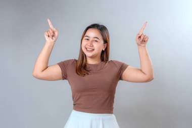 Her iki işaret parmağıyla yukarıya doğru gülümseyen neşeli genç bir kadın heyecan ve pozitiflik gösteriyor. Promosyon, reklam ve fotokopi alanı tasarımları için mükemmel.