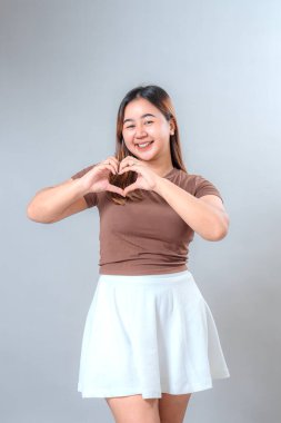 Elleriyle kalp şekli oluşturan gülümseyen genç bir kadın sevgi, nezaket ve pozitifliği ifade ediyor. Onun mutlu yüz ifadesi reklam ve yaşam tarzı temaları için ideal..