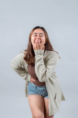 Samimi bir süveter giyen genç bir kadın yürekten güler, eli ağzını kapatır, tarafsız bir arkaplanda gerçek bir neşe ve eğlence ifade eder..