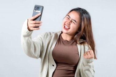 Genç bir kadın, elinde akıllı telefonuyla sevinçle kutlama yapar. Heyecanını ve zaferini tarafsız bir arkaplanda ifade eder..