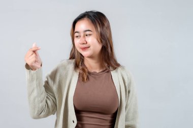 Genç bir kadın, genellikle sevgi ve şefkat ile ilişkilendirilen neşeli bir el hareketi yaparken ışıl ışıl gülümser. Samimi bir süveter giyiyor. Tarafsız bir zemine karşı neşeli ve dostane bir hava yayıyor.