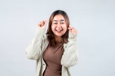 Genç bir kadın neşe dolu bir sürpriz yapar, gözleri açıktır ve elleriyle hareket ederken yüzünde bir gülümseme olur. Samimi bir süveter giyerek, heyecan ve mutluluğu simgeliyor..