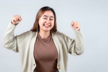 Genç bir kadın coşkulu bir sevinçle kutluyor, yumruklarını havaya kaldırıyor ve gülüyor. Bir kazak giyiyor, neşeli bir ifade takınıyor ve gülümsüyor. Zafer ve heyecan taşıyor..