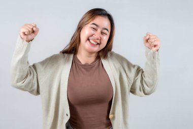 Genç bir kadın coşkulu bir sevinçle kutluyor, yumruklarını havaya kaldırıyor ve gülüyor. Bir kazak giyiyor, neşeli bir ifade takınıyor ve gülümsüyor. Zafer ve heyecan taşıyor..