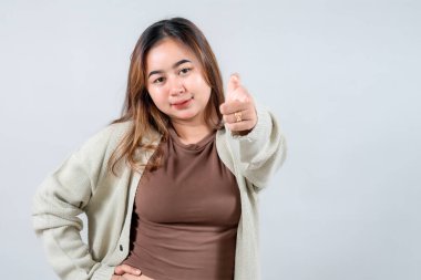 Genç bir kadın, kendine güvenen ve çekici bir ifadeyle doğrudan kameraya bakar, rahat bir kazak giyer. Tarafsız bir arkaplanda izleyiciyle bağlantı kuruyor..