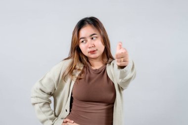 Genç bir kadın, kendine güvenen ve çekici bir ifadeyle doğrudan kameraya bakar, rahat bir kazak giyer. Tarafsız bir arkaplanda izleyiciyle bağlantı kuruyor.