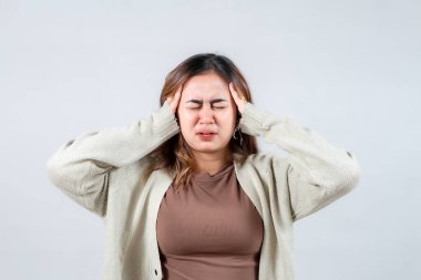 Genç bir kadın, acı ve ıstırabı ifade eden yüzünü ellerinin arasında tutuyor. Samimi bir süveter giyerek basit bir geçmişe karşı güçlü bir baş ağrısı ya da duygusal stres hissi taşıyor..