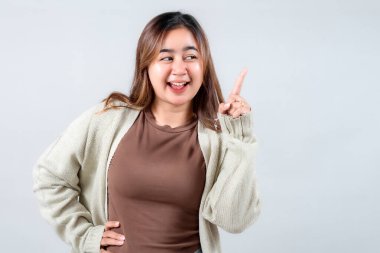 Samimi bir süveter giyen neşeli genç bir kadın, neşeli bir ifadeyle yukarıya bakıyor. Tarafsız bir arkaplan karşısında heyecanını ve yaratıcılığını gösteriyor..