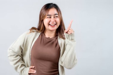 Samimi bir süveter giyen neşeli genç bir kadın, neşeli bir ifadeyle yukarıya bakıyor. Tarafsız bir arkaplan karşısında heyecanını ve yaratıcılığını gösteriyor..