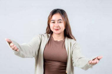 Samimi bir süveter giyen neşeli genç bir kadın kollarını kucaklamak için açar. Tarafsız bir arkaplana karşı samimiyet, hoş geldin ve sevgi ifade eder..