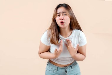 Endişeli bir ifadesi olan genç bir kadın, sanki bir şey açıklıyormuş gibi el kol hareketi yapıyor, yumuşak bir bej arka plana yaslanıyor, duygularını ve bağlılığını iletiyor..