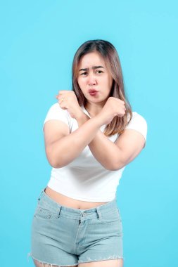 Beyaz tişörtlü genç bir kadın kollarını kavuşturur ve dudaklarını büzer, parlak mavi bir arka plana karşı, tasvip ya da şüphecilik taşır, açık bir mesaj verir