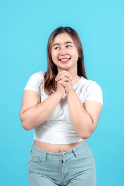 Heyecanlı genç bir kadın elini sıkar, coşkulu mavi bir arka plana sevinçle ışıldar, mutluluk ve beklenti ifade eder.