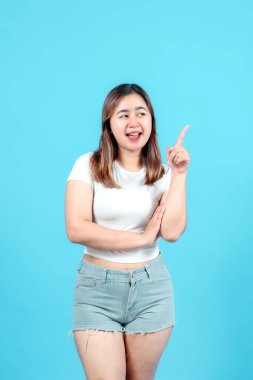 Gülümseyen genç bir kadın tek eliyle yukarıyı işaret ederek parlak mavi bir arka plana karşı bir fikir ya da yön öneriyor..