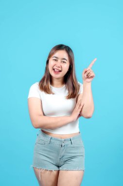 Gülümseyen genç bir kadın tek eliyle yukarıyı işaret ederek parlak mavi bir arka plana karşı bir fikir ya da yön öneriyor..