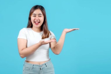 Gülümseyen genç bir kadın bir ürün ya da fikir sunuyor, mavi bir arka plana karşı elini açık tutuyor..