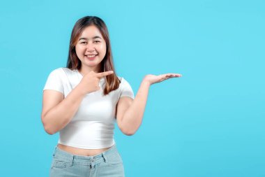 Gülümseyen genç bir kadın bir ürün ya da fikir sunuyor, mavi bir arka plana karşı elini açık tutuyor..