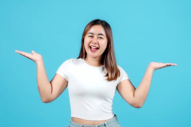 Neşeli genç bir kadın iki elini de uzatıyor, iki seçenek sunuyor ya da ürünleri mavi arka planla karşılaştırıyor..