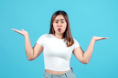 Beyaz ekin bluzlu genç bir kadın şaşırmış bir yüz ifadesiyle kafa karışıklığı gösterir, her iki eliyle parlak mavi bir arka plana işaret eder.