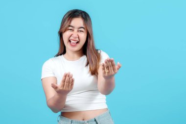 Neşeli genç bir kadın, gülüyor ve elleriyle şakacı hareketler yapıyor, parlak mavi bir arka planda, sıcaklık ve dostluk saçıyor..