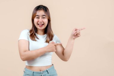 Neşeli genç bir kadın her iki tarafı da neşeyle gösterirken geniş bir gülümseme, yumuşak bir bej arka plan, neşe ve coşku saçıyor..