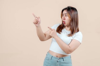 Neşeli, gülümseyen ve farklı yönleri işaret eden genç bir kadın. Yumuşak bir bej arka plan, coşku ve pozitiflik saçıyor..