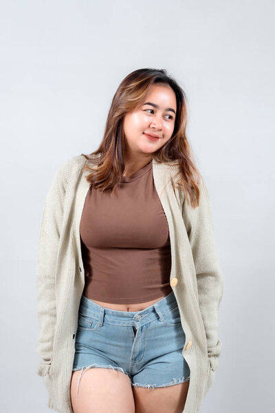 Молодая женщина в уютном свитере и джинсовых шортах уверенно улыбается, демонстрируя непринужденный и стильный вид на нейтральном фоне.