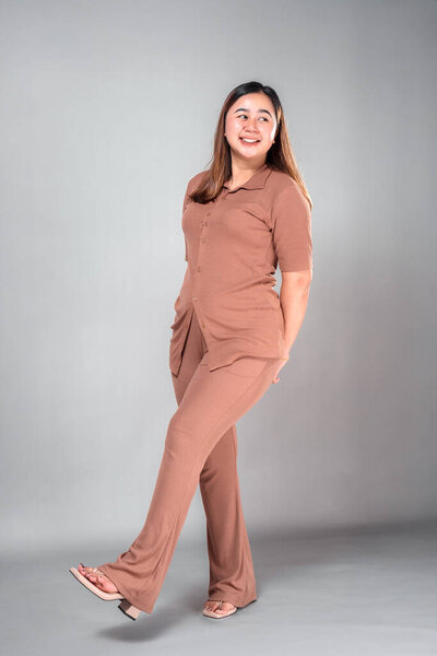 Cheerful young Asian woman smiling brightly while looking to the side, lifting one leg playfully. Her joyful expression conveys positivity, friendliness, and natural charm.