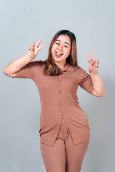 Cheerful young Asian woman showing double peace signs with a big smile and joyful expression, conveying positivity, happiness, and playful youthful energy.