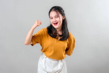 Mutlu, genç Asyalı bir kadın, kendine güven ve başarı göstererek parlak bir gülümsemeyle zafer yumruğu sallıyor. Enerji dolu yüz ifadesi kutlama veya motivasyon temaları için mükemmel.