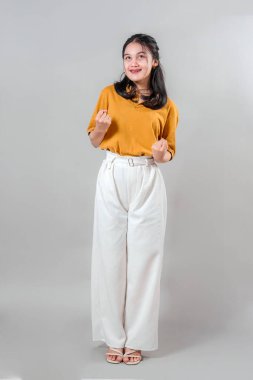 Genç Asyalı bir kadın zaferle dolu bir duruşta kendine güvenen yumruklarıyla gülümsüyor. Neşeli yüz ifadesi başarı teması için heyecan, coşku ve pozitif enerji yayıyor..