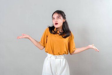 Asyalı genç bir kadın dramatik bir ifadeyle omuzlarını kaldırarak kaldırarak bakıyor ve omuzlarını silkiyor. İnançsızlığını ve belirsizliğini mizahi bir şekilde ifade ediyor..