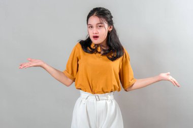 Kafası karışmış genç Asyalı kadın ellerini kaldırarak omuzlarını silkiyor ve şaşırmış yüz ifadesi, doğrudan kameraya bakıyor. Belirsizlik, soru ya da şüphe gibi kavramlar için mükemmel..